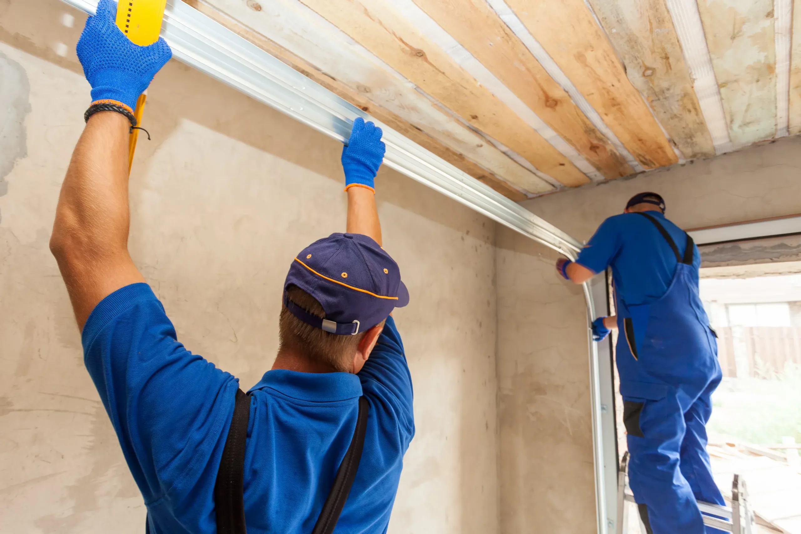 men-installing-garage-door-rails Garage doors installation. Workers installing Post Rail and Spring Installation / Assembly.