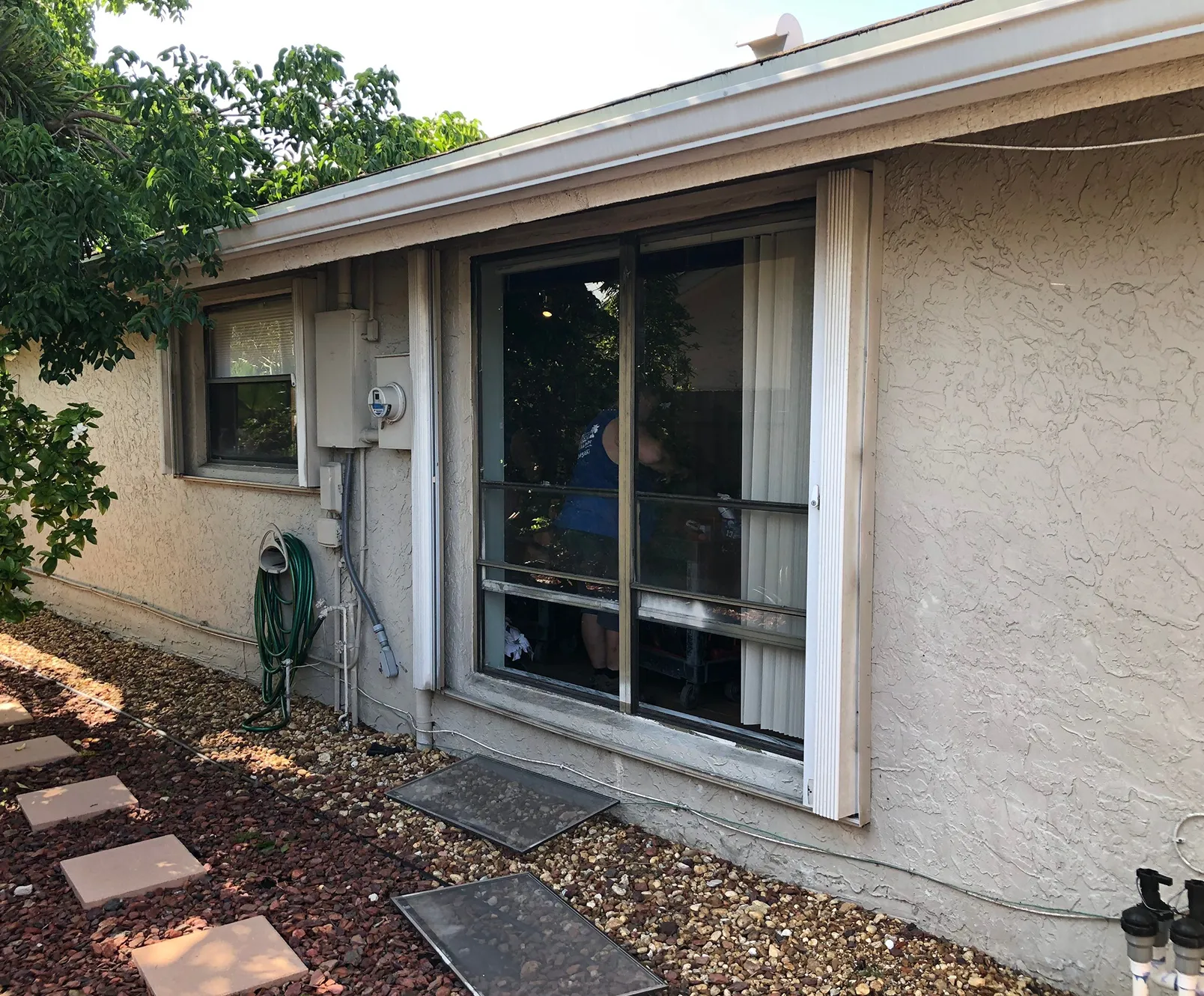 exterior view of a single-story home's back window with sliding glass and pebble pathway